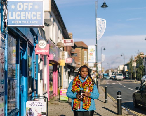 Woman with a brightly coloured scarf walking down a local high street holding a reusable coffee cup