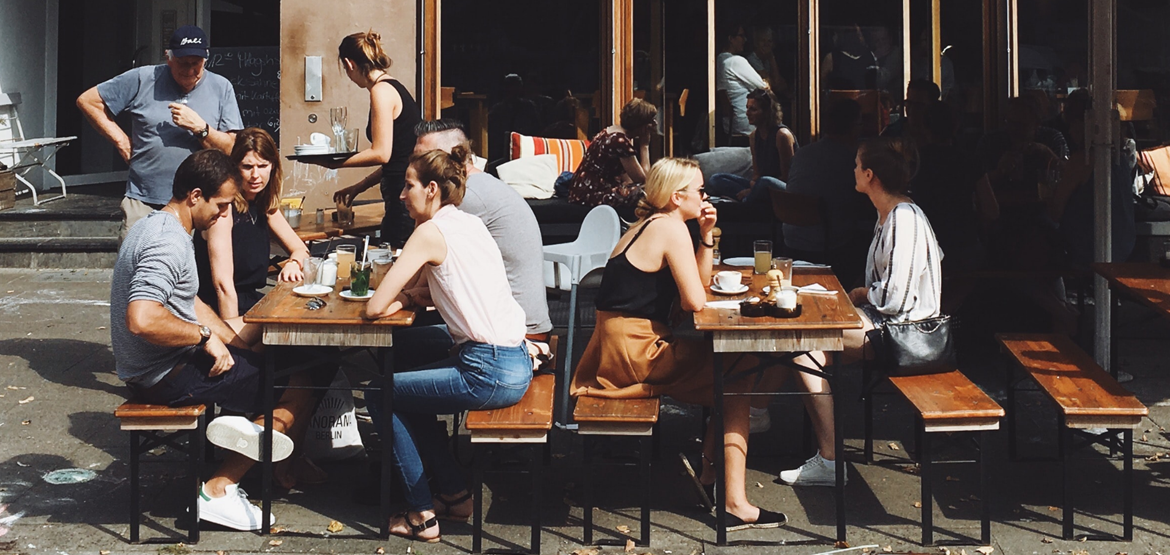 Groups of people sitting around outside tables in a social setting