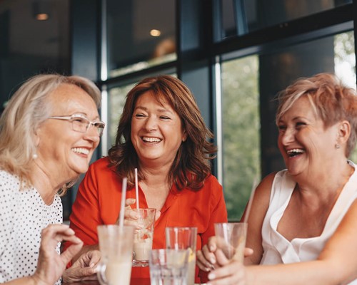 Three older women sitting around a table drinking coffee and laughing together