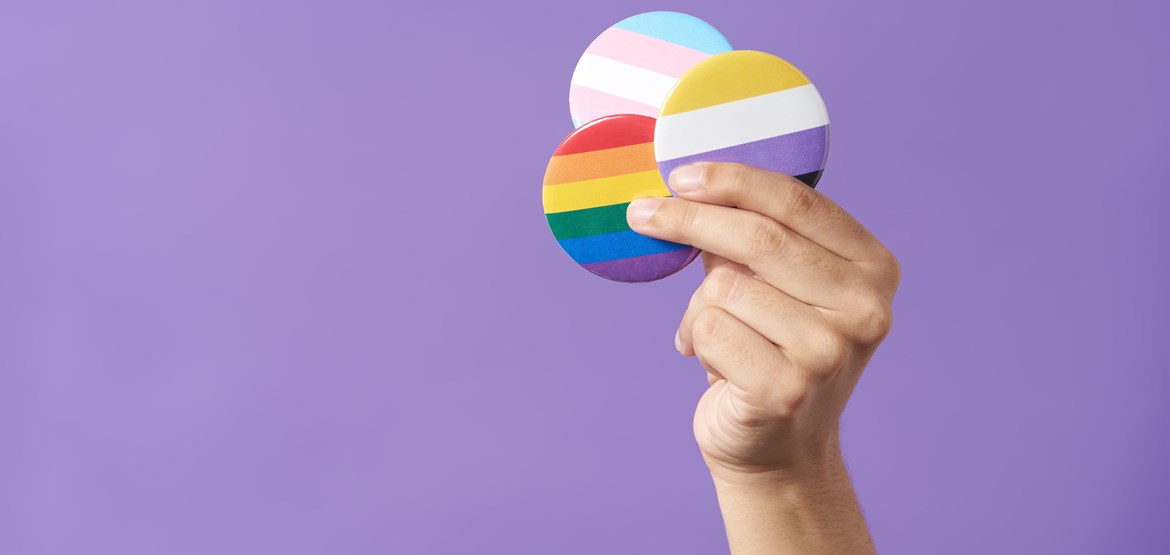 A person holding up pins with the transgender, non-binary and LGBT+ flags