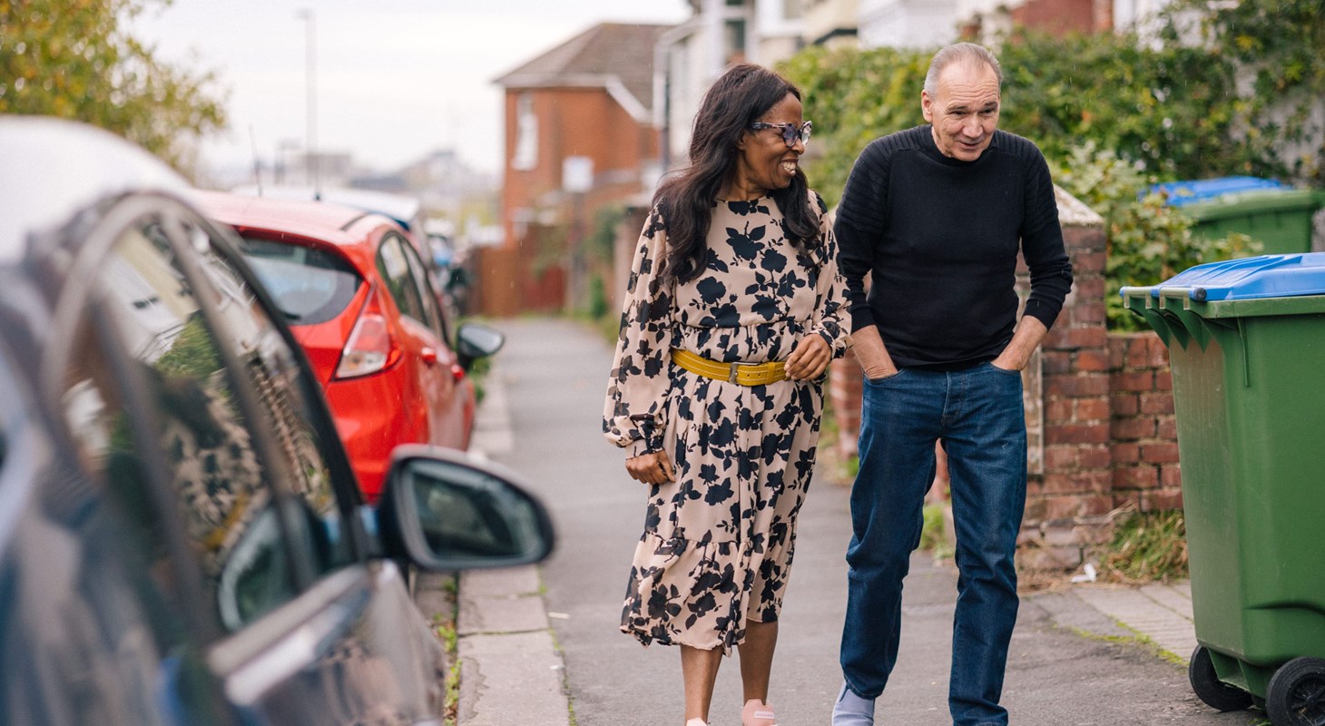 A man and a woman walking down a suburban street talking