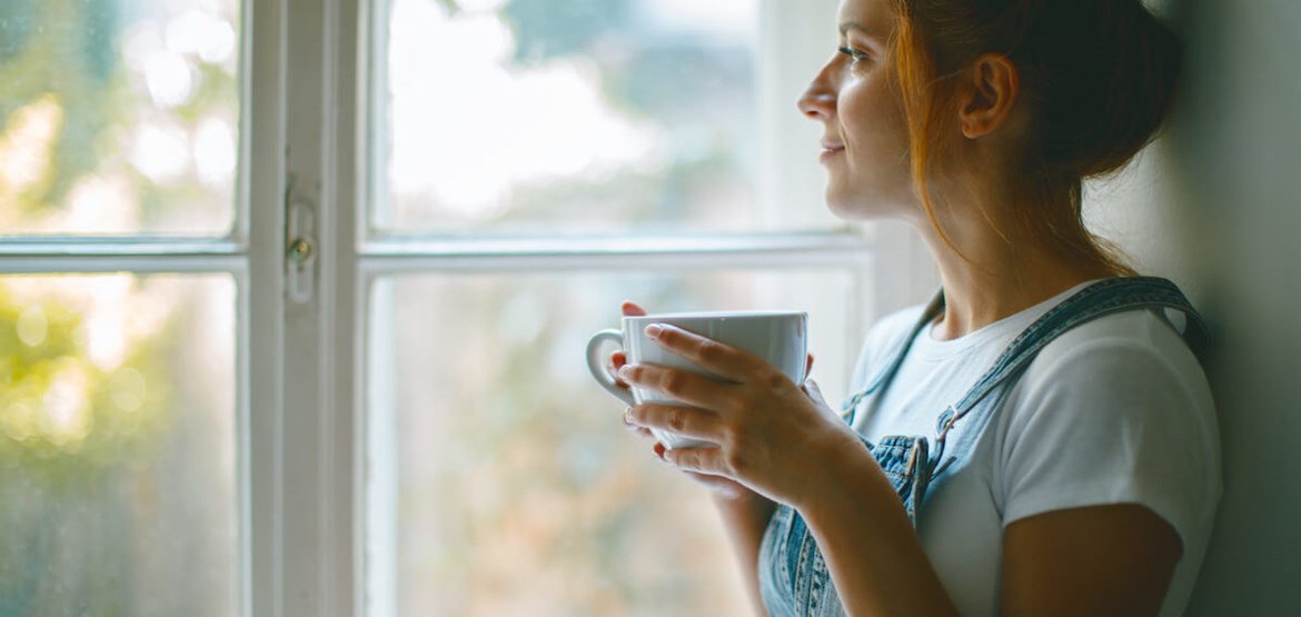 Woman looking out of window holding a mug