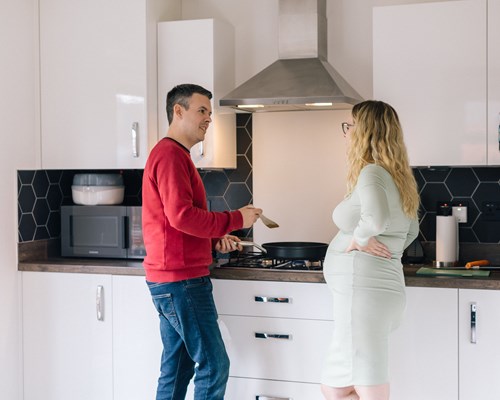 A pregnant woman and man standing in a kitchen talking and cooking