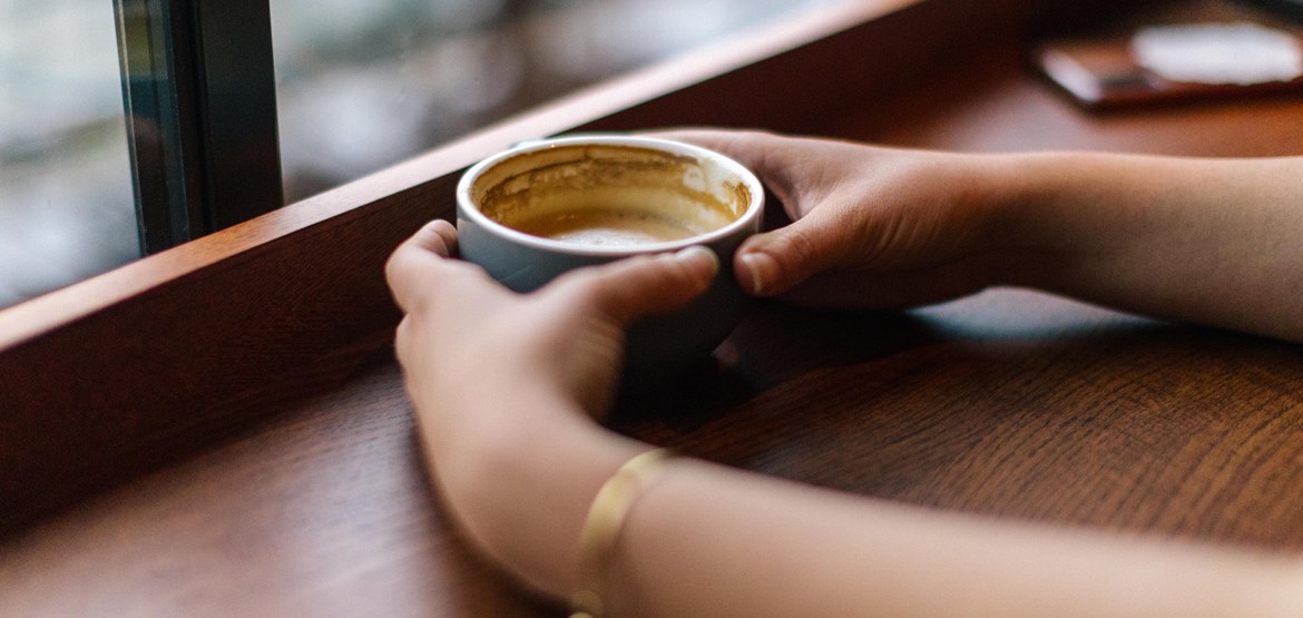 Hands holding a cup at a window seat in a café