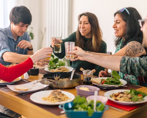 Group of people saying cheers around a dinner table with food