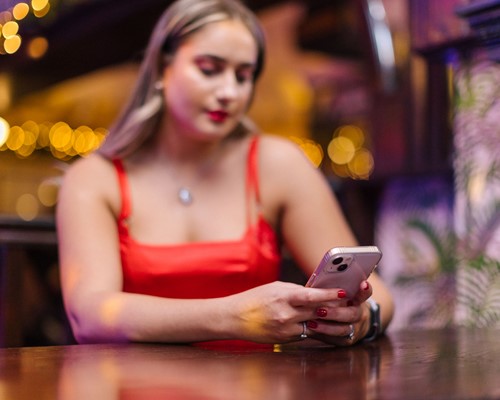 Woman sitting alone on her phone in social setting looking forlorn