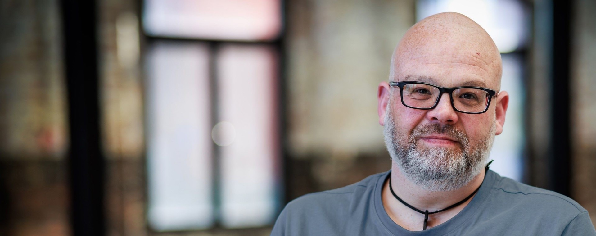 A man with a bald head, short beard and glasses looking into the camera with a slight smile