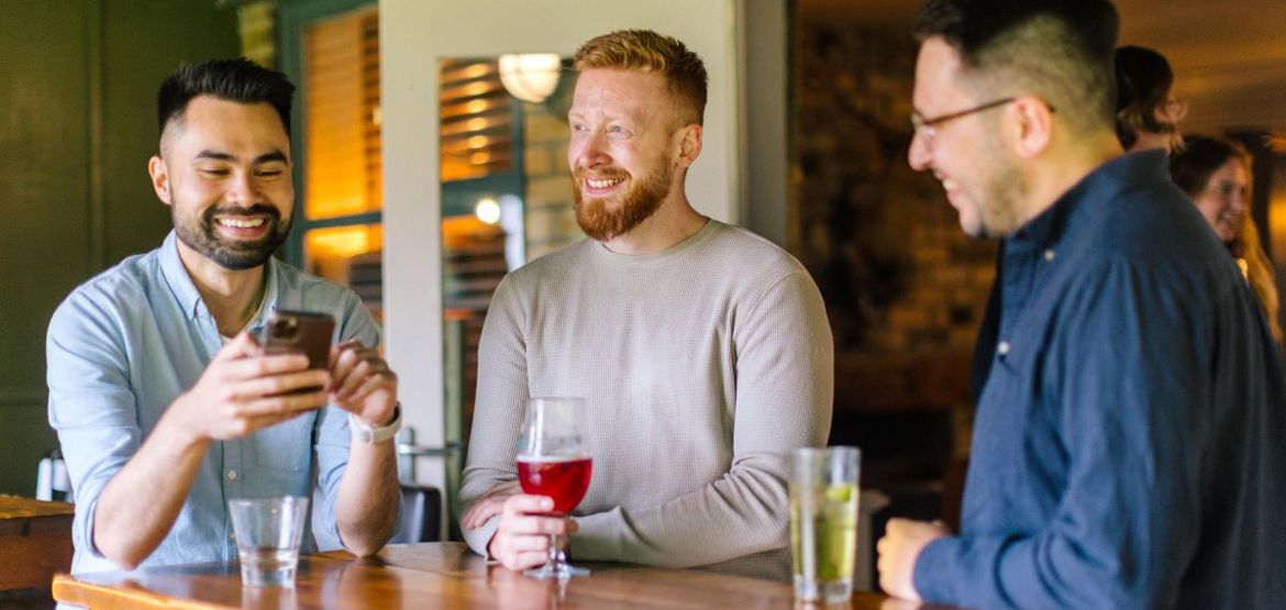 Person stood by two friends and checking their phone in a pub.