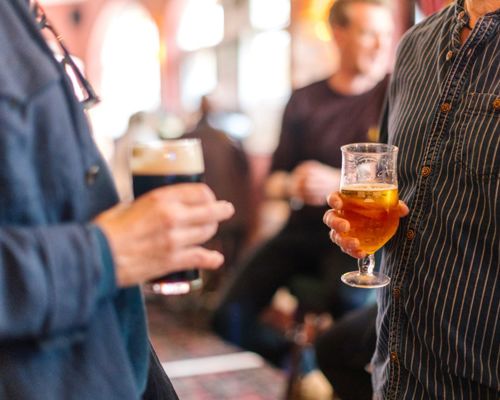 Close up of two people holding pints in pub.