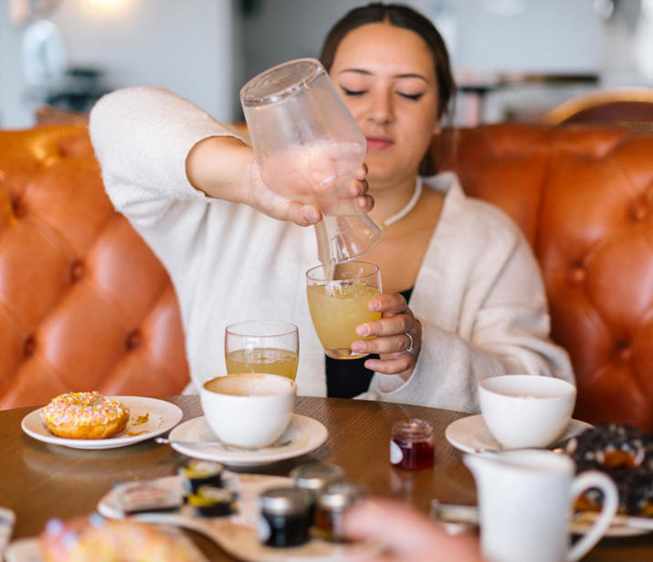 Woman sitting at a large round table pouring some juice from a jug