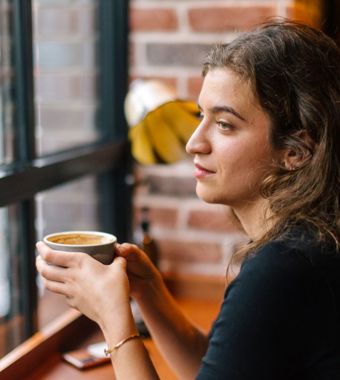 Person sat by window, holding a coffee. 