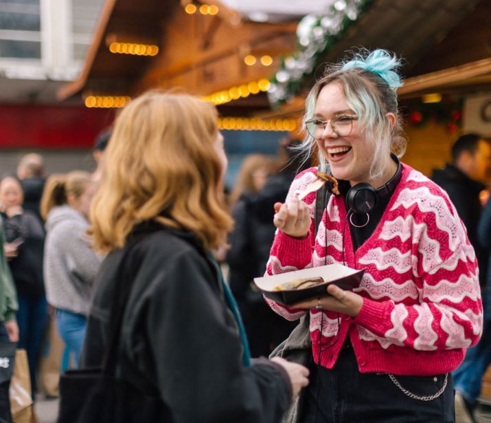 Two friends, smiling and eating churros at a Christmas market.
