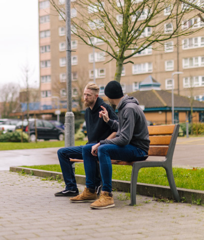 Two men sitting on a bench in an urban area having a serious conversation
