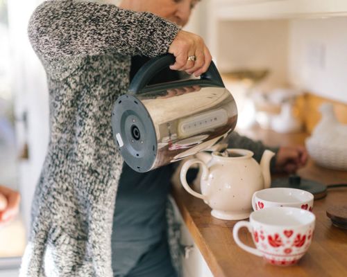 Person filling up teapot with water from a kettle.