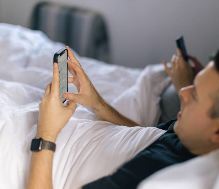 A couple laying in bed, both scrolling on their phones