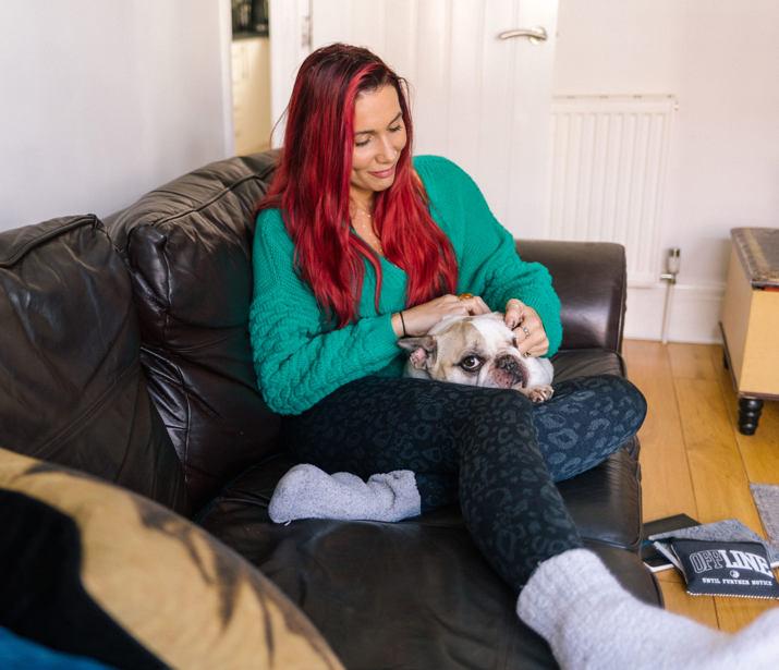 Woman with red hair reclining on sofa with her dog in her lap