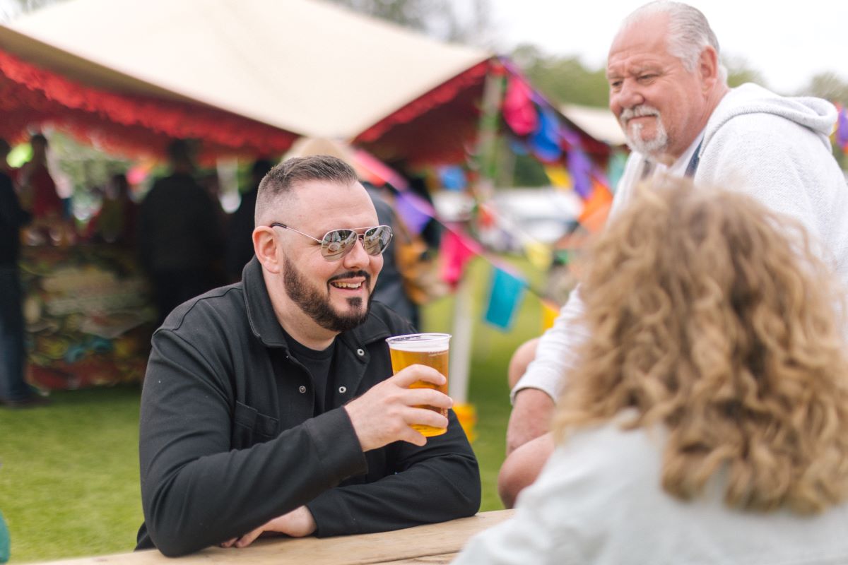 Person drinking beer in front of festival tent.