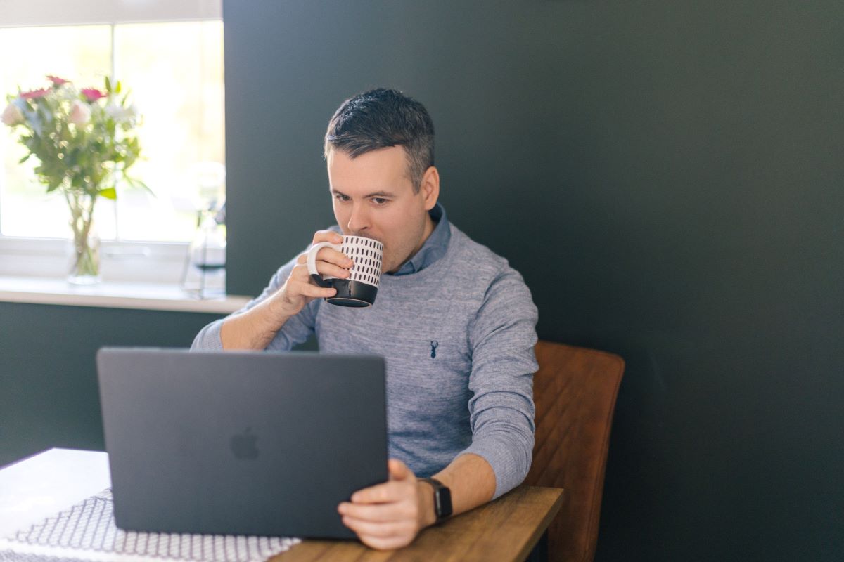 Person sipping from mug and looking at laptop.