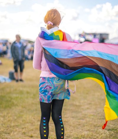 Person wearing pride flag as cape, with rainbow coloured hearts on the back of their legs.