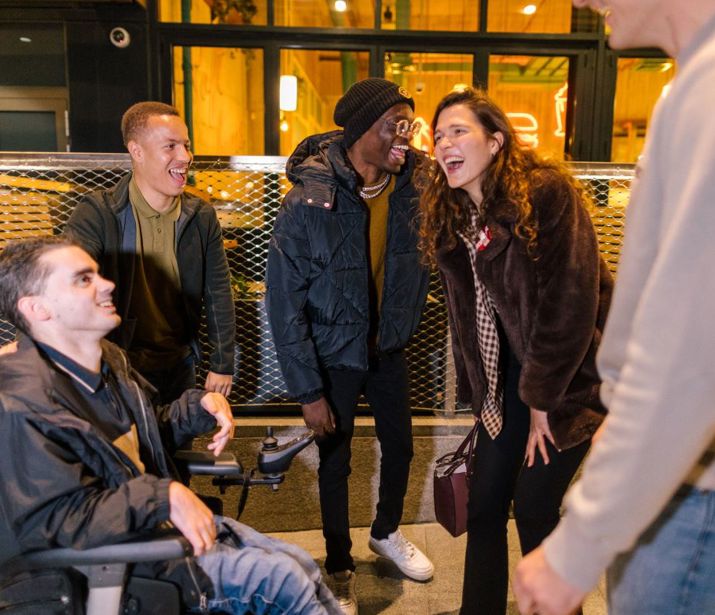 Group of people laughing outside a bar at night.