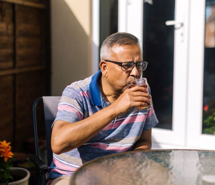 Person sat outside at a garden table, drinking a beer.