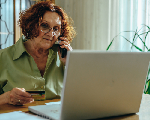 Older woman sat at a table with a laptop in front of her holding a credit card