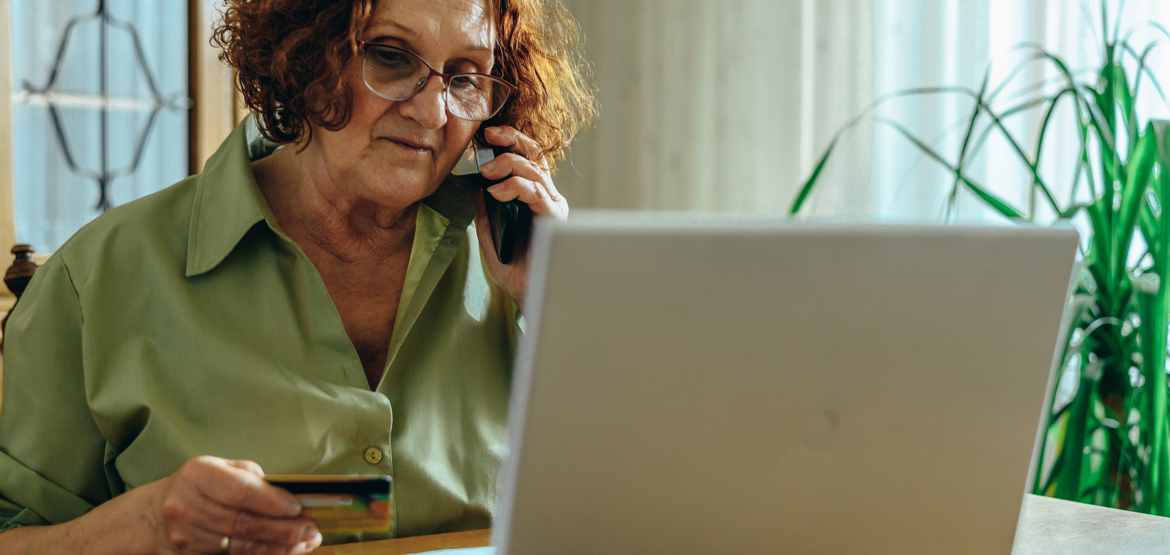 Older woman sat at a table with a laptop in front of her holding a credit card