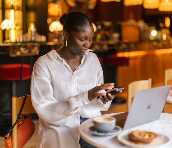 Person sat in cafe with laptop and also typing on their phone.