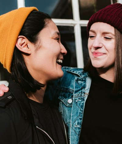 Two women, wearing beanies, looking at each other and smiling