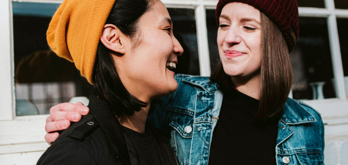 Two women, wearing beanies, looking at each other and smiling