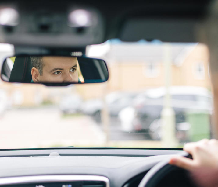 A man in a car with his face visible in the rear view mirror