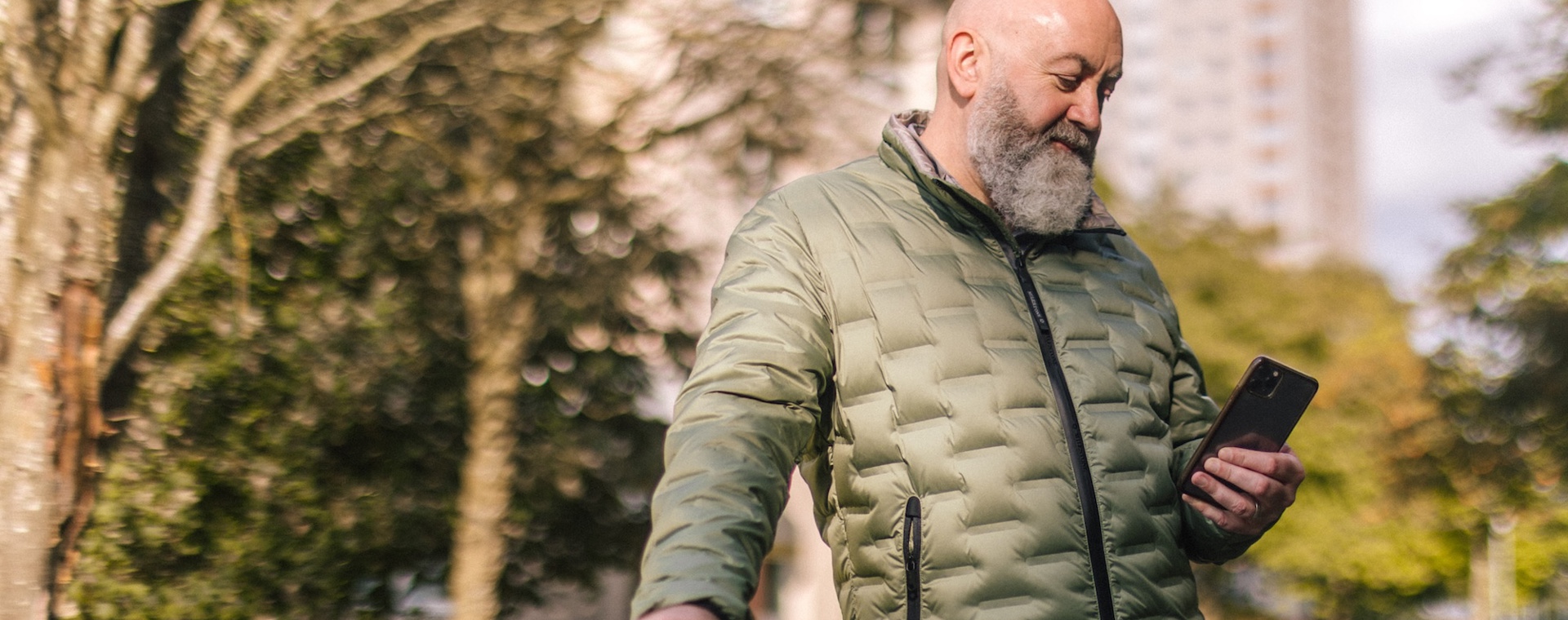 A white man with a beard looking at his phone in front of housing estate