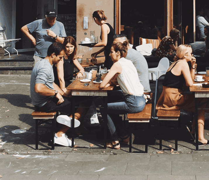 Groups of people sitting around outside tables in a social setting