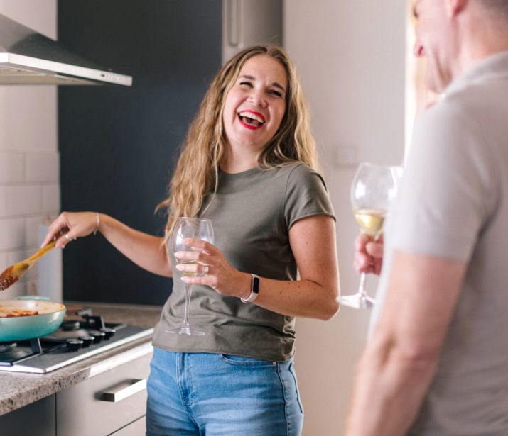 Couple cooking dinner, holding wine glasses and laughing.