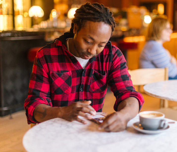 Man sitting at a café table with a cup of coffee, scrolling on his phone