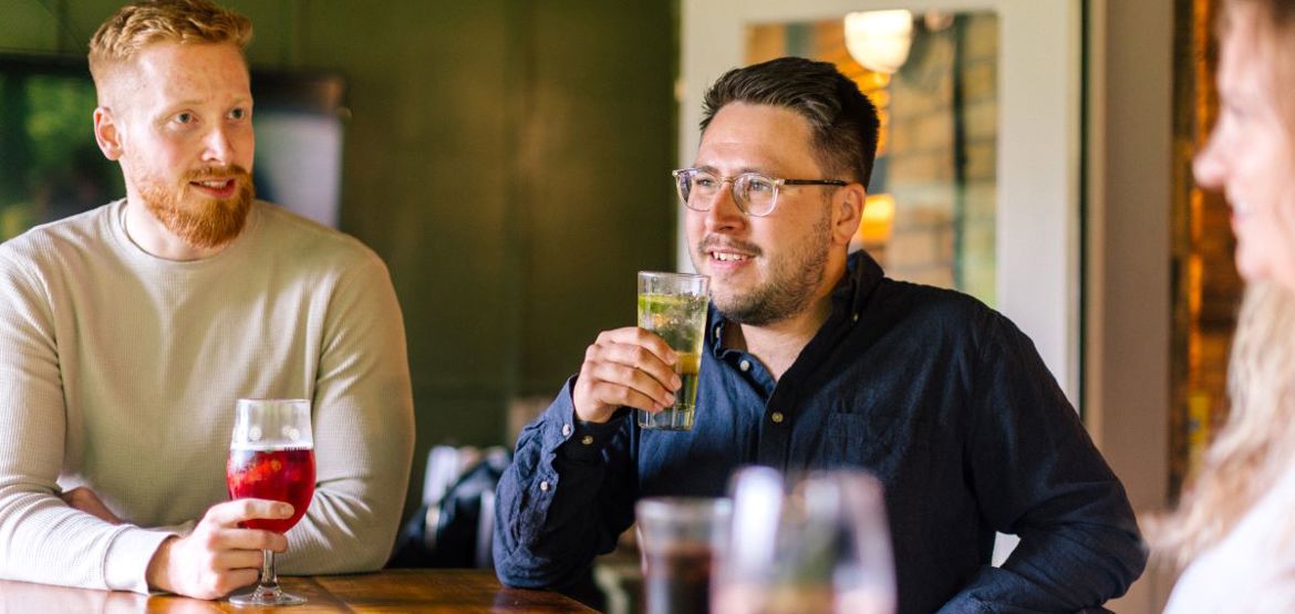 Two people stood at a table in a pub, having drinks.