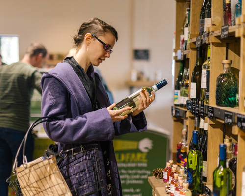 Woman in a shop holding a bottle and looking at the label