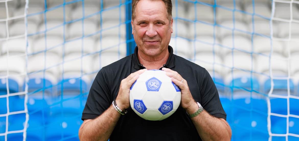 Footballer David Seaman stood in front of a football net holding a blue and white football