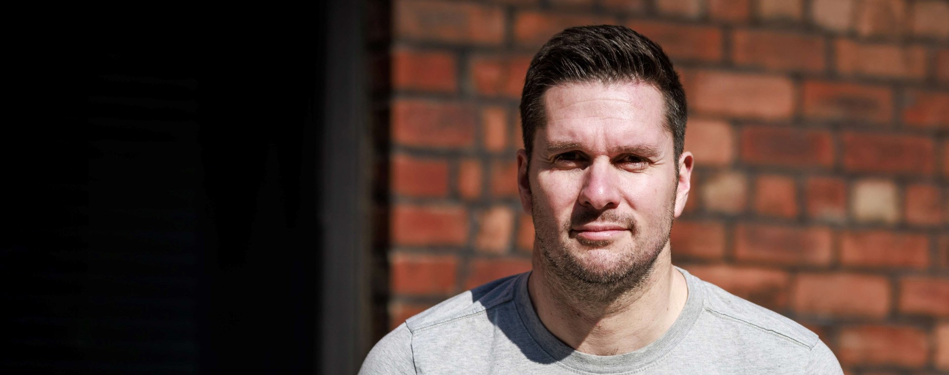 A man with short hair and stubble looking into the camera with a slight smile