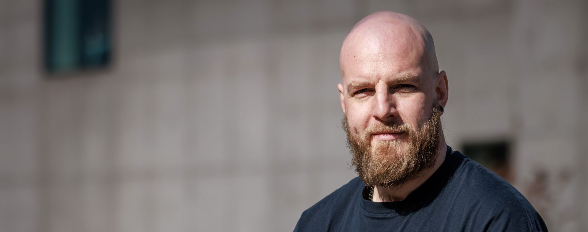 A man with a shaved head and mid length beard looking into the camera with a slight smile