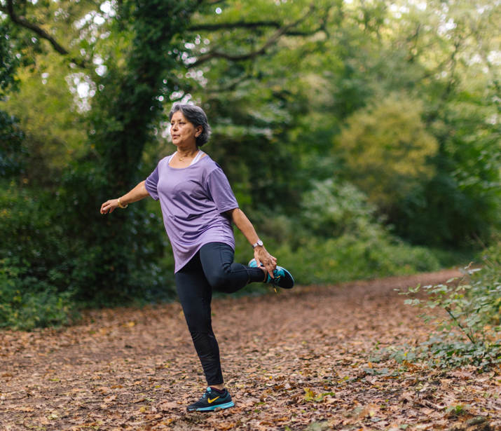 Woman lifting her leg up to stretch in a woodland setting