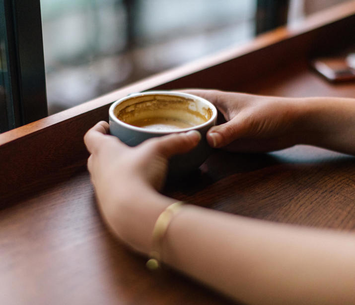 Hands holding a cup at a window seat in a café