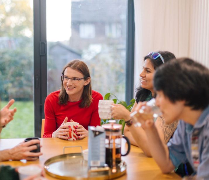 Friends gathered around a kitchen table chatting and drinking coffee.