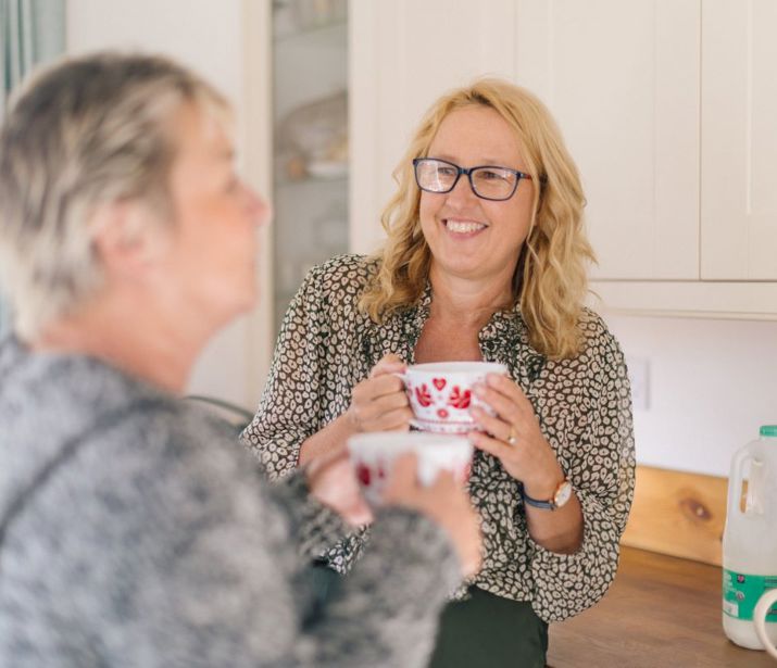 Two friends holding mugs in kitchen.