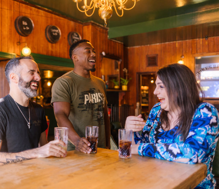 Three people sitting and standing around a high table, laughing and enjoying socialising