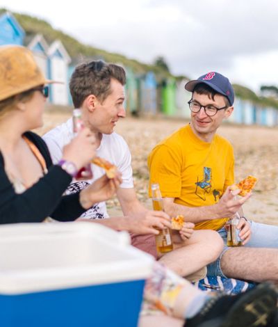 Group eating pizza on a pebble beach.